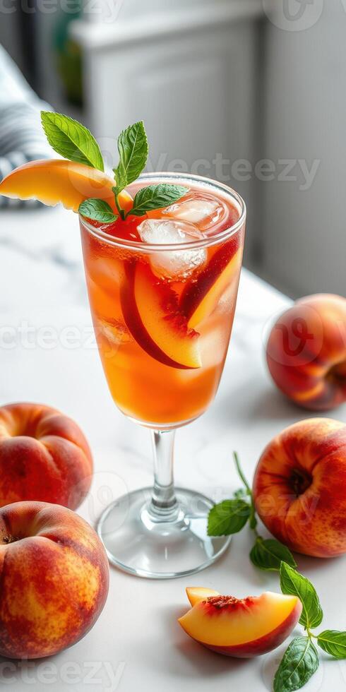 Refreshing peach iced tea served in a clear glass with mint leaves and fresh peaches on a marble countertop photo