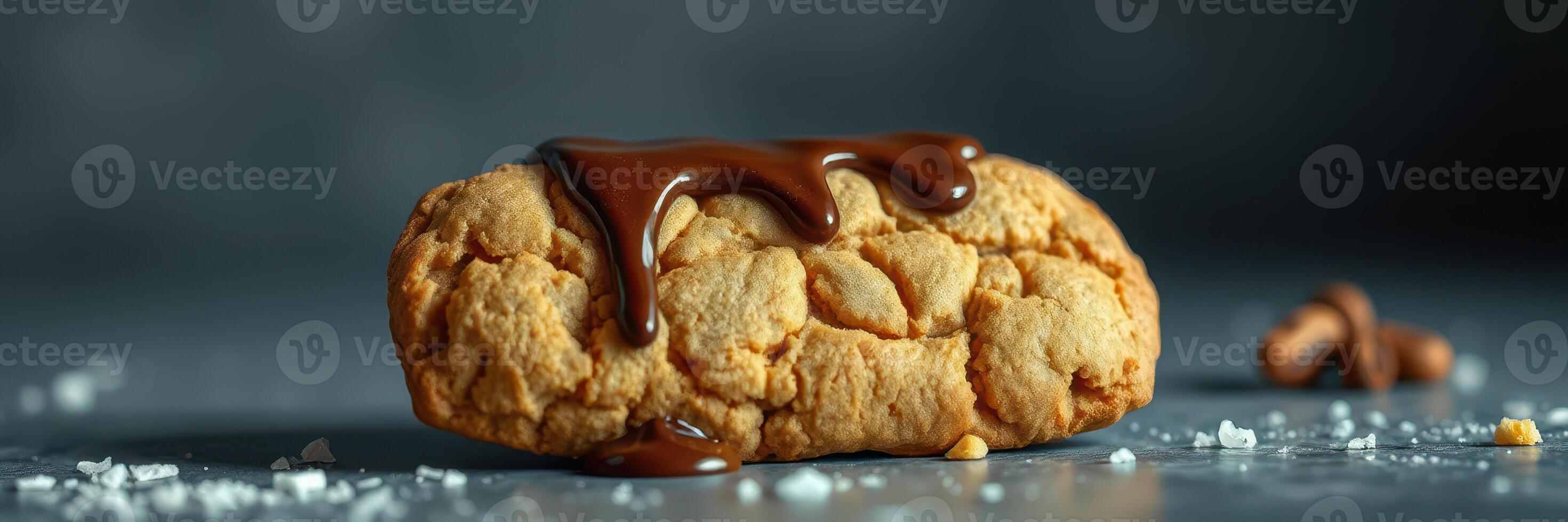 Soft cookie topped with chocolate drizzle placed on a dark surface with sugar crystals scattered around photo