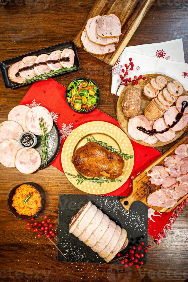 A table filled with Christmas products such as roasted turkey, pork leg, ham, and various holiday-season pickled accompaniments. photo