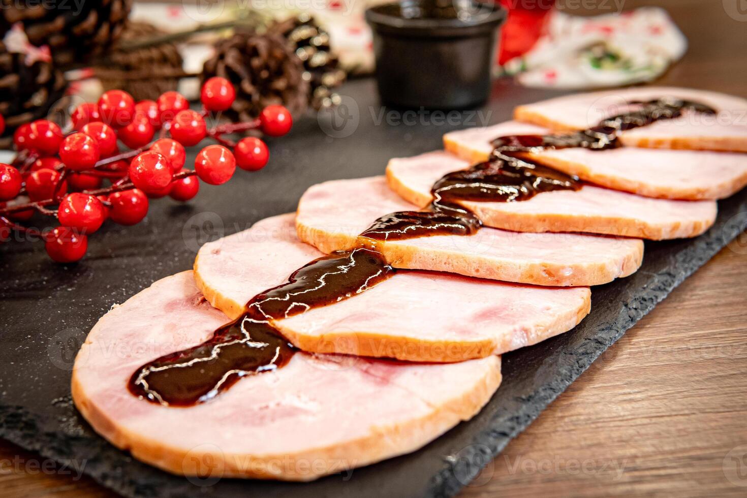 Slices of Christmas pork leg pernil with plum sauce and festive decorations on a wooden board. photo
