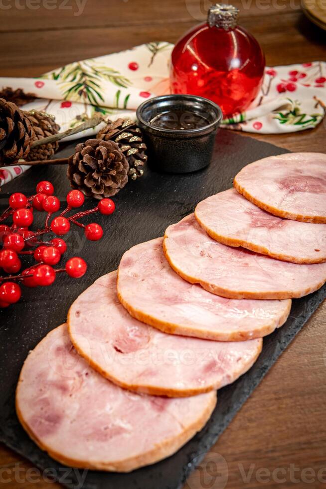 Slices of Christmas pork leg pernil with plum sauce and festive decorations on a wooden board. photo