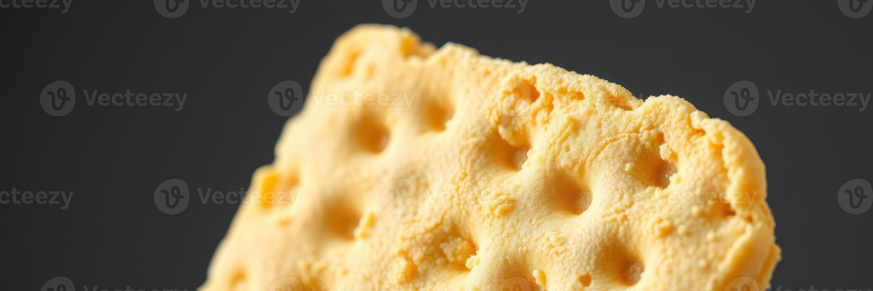 Delicious yellow cheese cracker displayed on a dark background, showcasing its texture and unique shape vividly photo