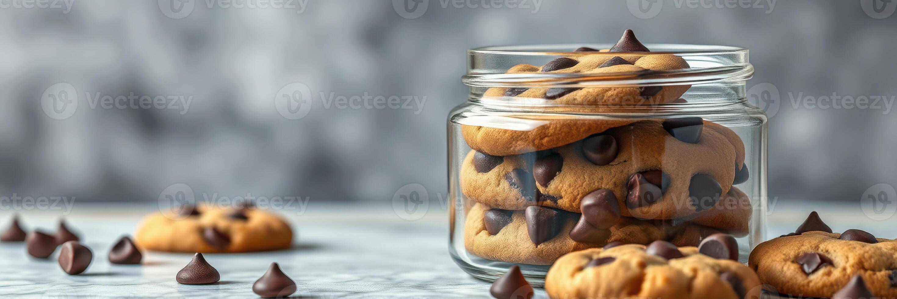 Delicious chocolate chip cookies arranged in a glass jar on a marble surface with some scattered on the side photo