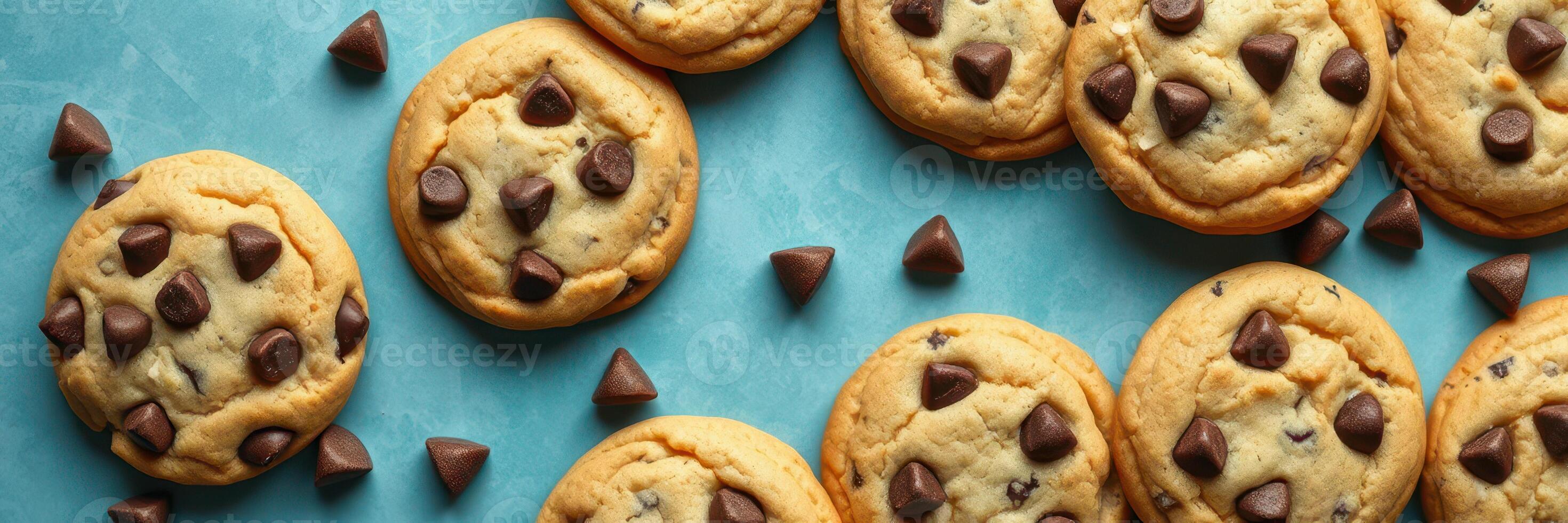 Freshly baked chocolate chip cookies arranged on a turquoise surface with chocolate chips scattered around photo