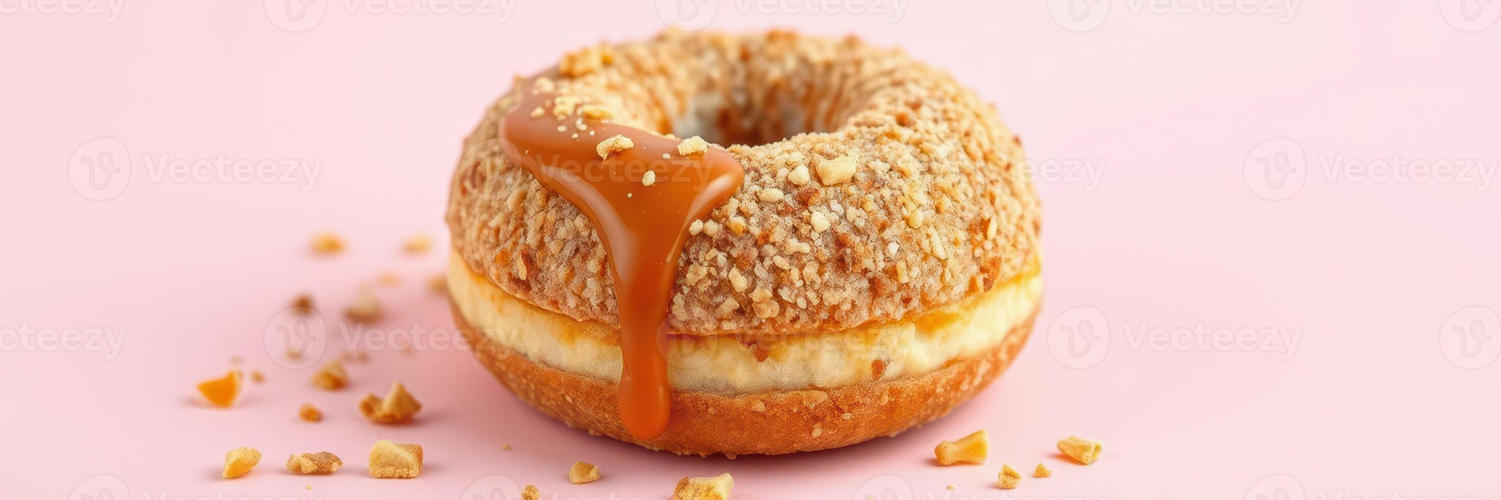 Delicious donut topped with crushed nuts and caramel drizzle on a pastel pink background photo