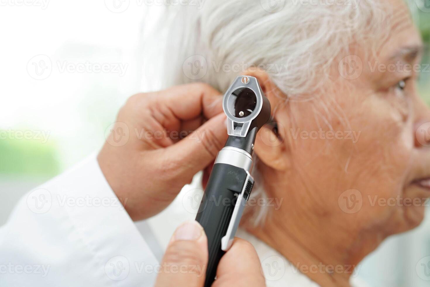 Otolaryngologist or ENT physician doctor examining senior patient ear with otoscope, hearing loss problem. photo