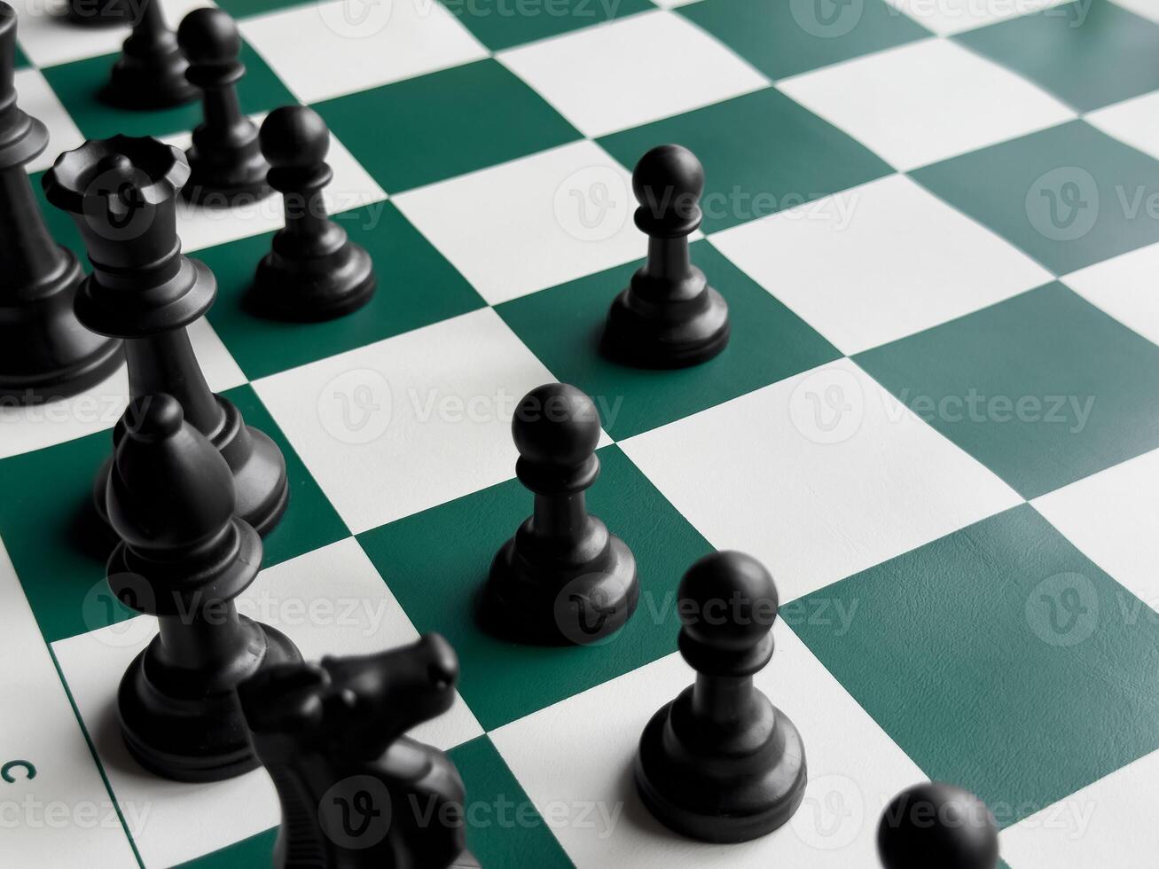 Strategic chess game on green and white board with black pieces photo