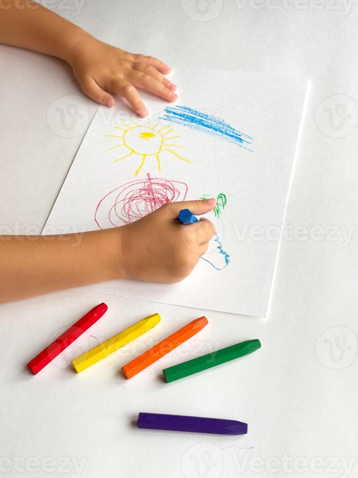 Childs colorful drawing of sun and clouds with crayons on white paper photo