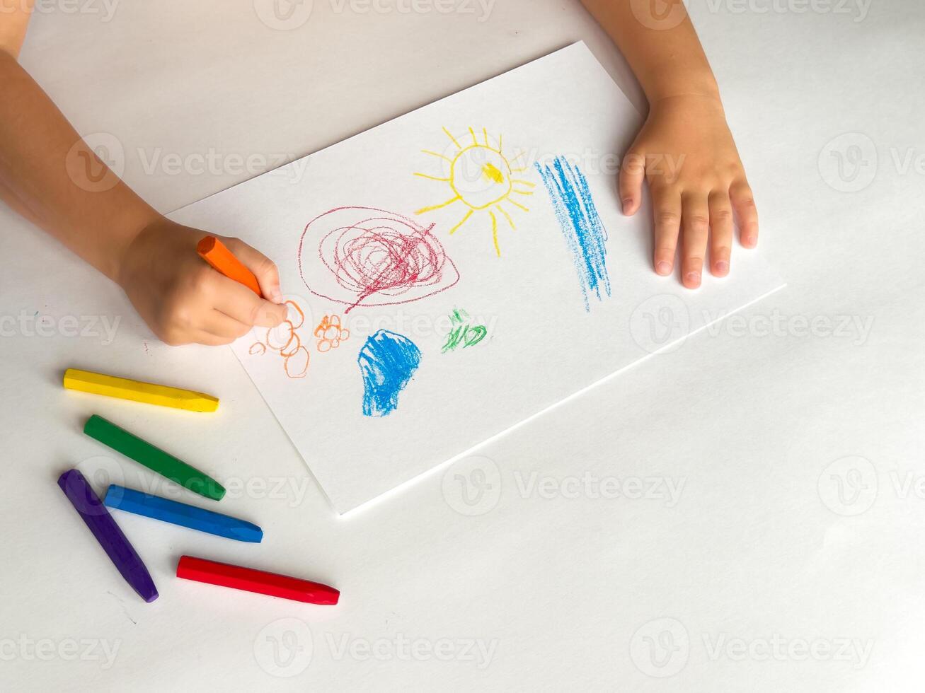 Child drawing with colorful crayons on white paper photo