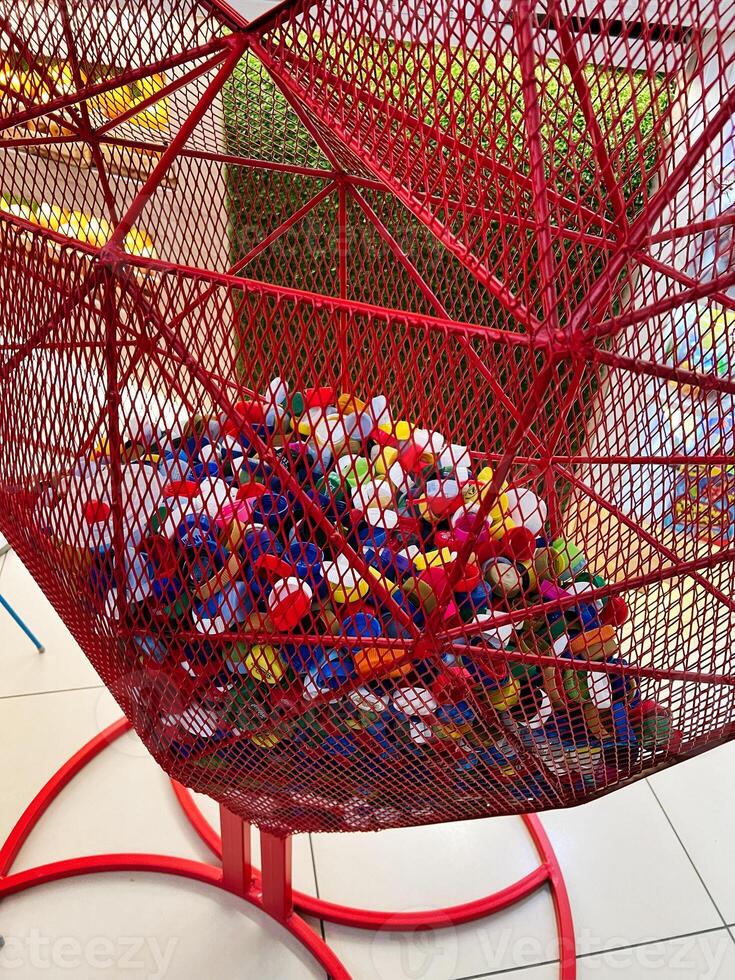 Red metal container holding colorful plastic bottle caps in a geometric design photo