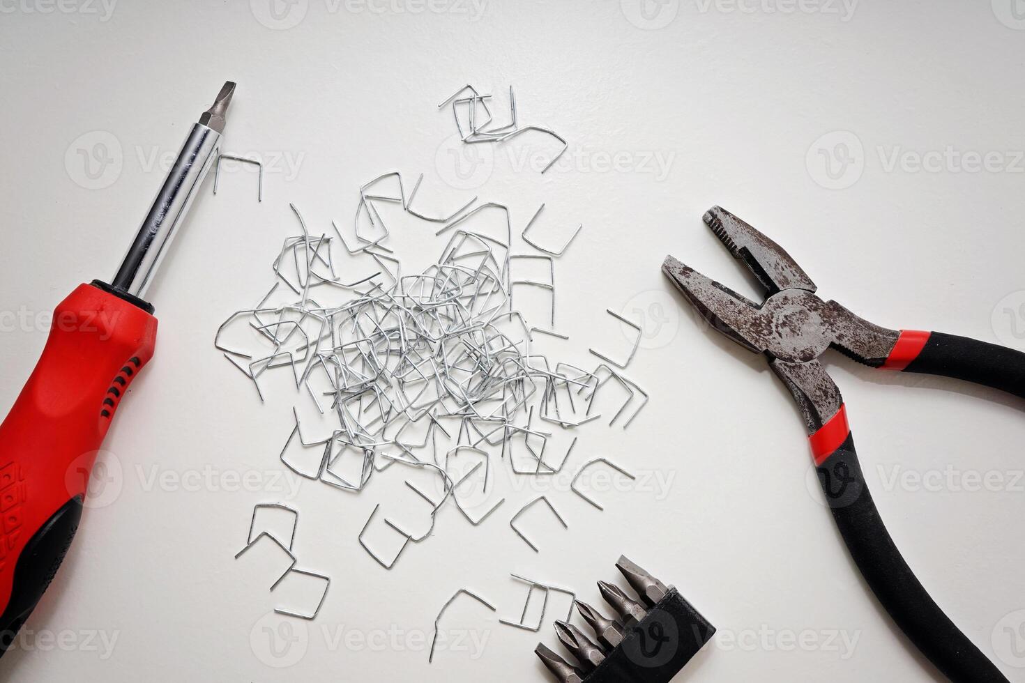 Screwdriver, Pliers, Bits, and Staples Arranged on White Surface with Copy Space. photo