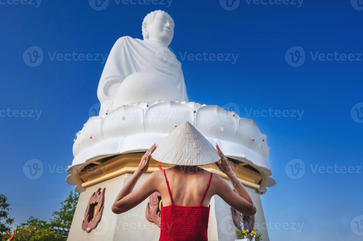portrait from the back of a tourist in a red dress and a traditional Vietnamese hat on the background of Buddha in a pagoda in Nha Trang photo