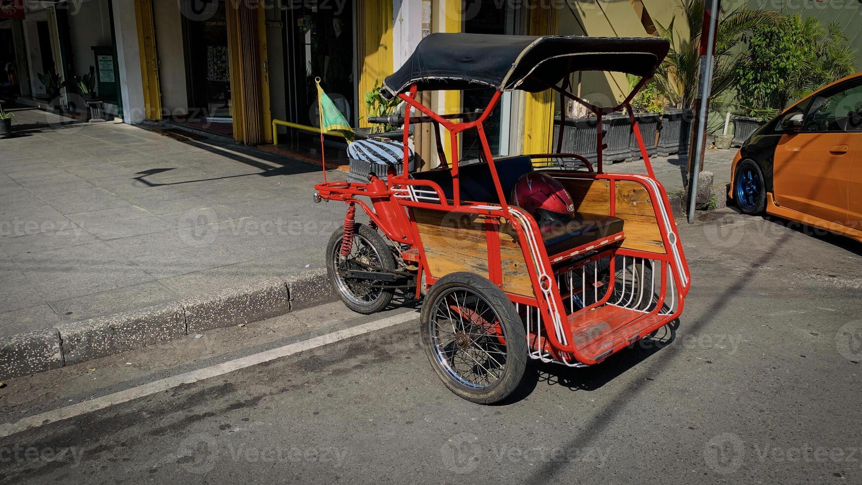 pedicab or rickshaw or locals calls it becak with a canopy is parked on a sunny street, reflecting a vibrant urban scene. The vehicle features a padded seat and unique design photo