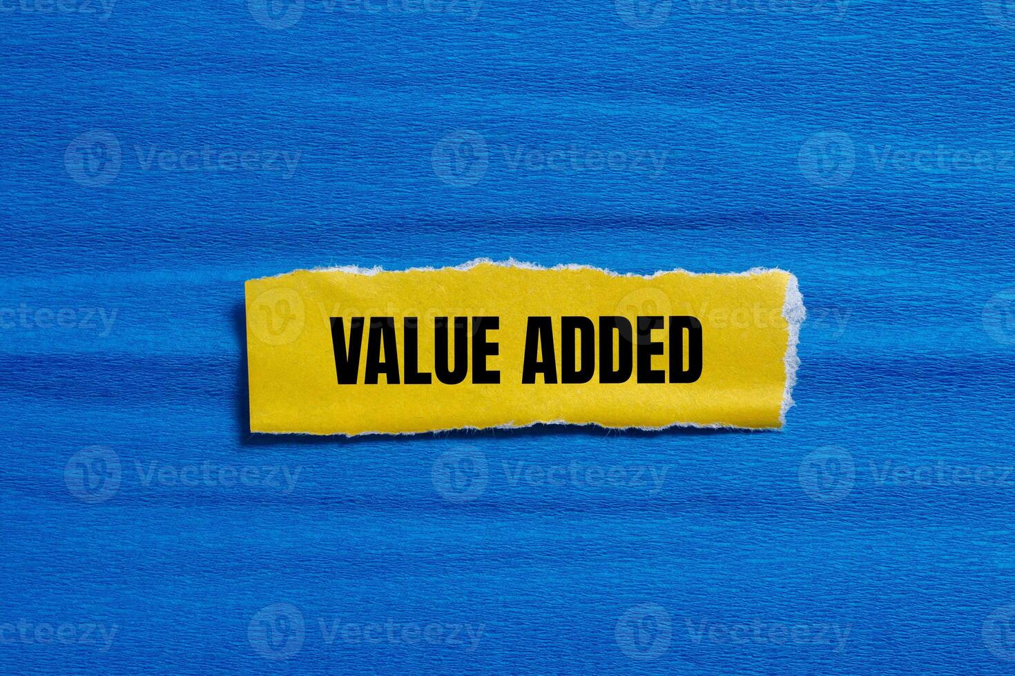 Value added message written on ripped torn yellow paper piece with blue background. Conceptual value added symbol. Copy space. photo