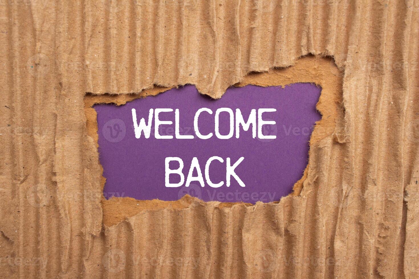 Welcome back message written on ripped torn cardboard paper with purple background. Conceptual welcome back symbol. Copy space. photo