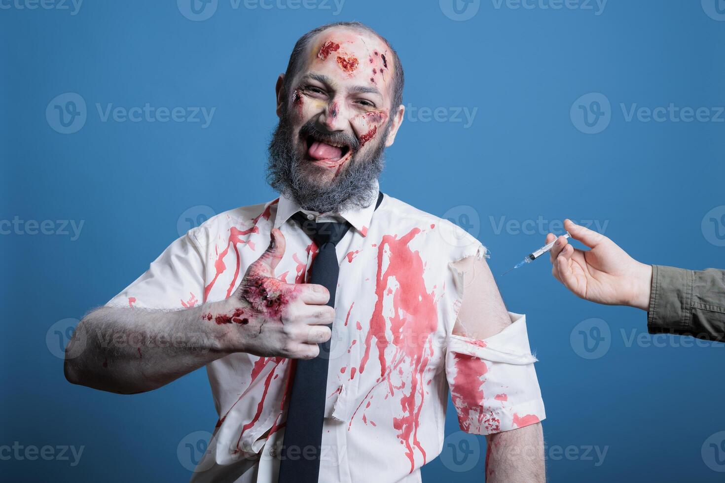 Cheerful man covered in blood and bruises receiving antidote serum after being attacked by feral animals, showing thumbs up sign. Hurt person getting remedy vaccine, studio background photo