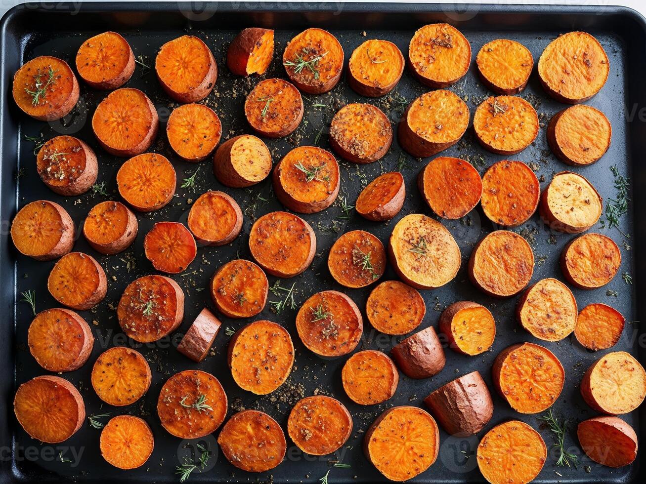 Freshly Sliced Sweet Potatoes Roasted to Perfection with Herbs and Spices on a Dark Baking Sheet Background photo