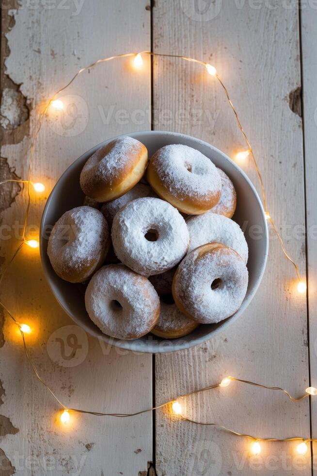 A Bowl Filled with Sweet Doughnuts Covered in Powdered Sugar and Surrounded by a String of Warm Lights on a Wooden Surface photo