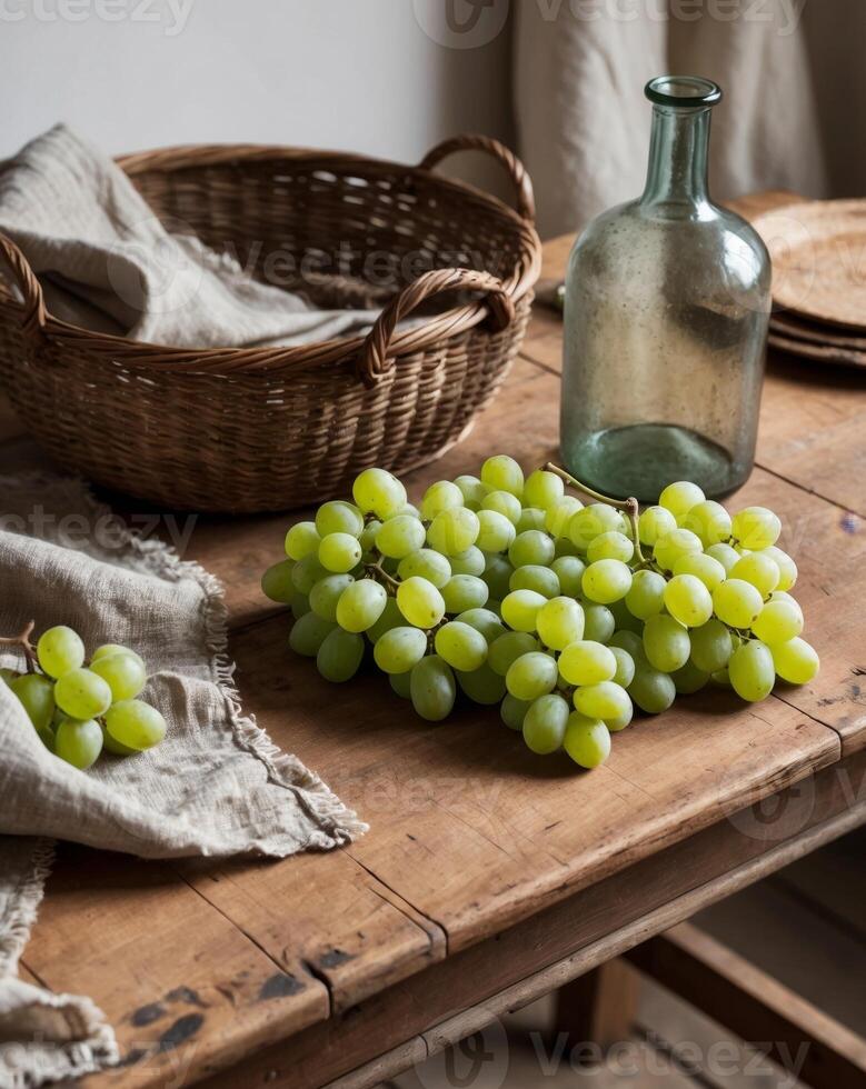 Fresh green grapes and a glass bottle create a rustic still life on an antique wooden table surrounded by earthy textures in a cozy setting photo
