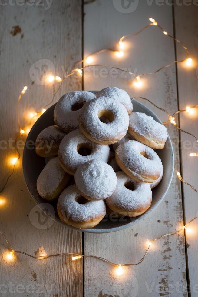 A Bowl Filled with Sweet Doughnuts Covered in Powdered Sugar and Surrounded by a String of Warm Lights on a Wooden Surface photo