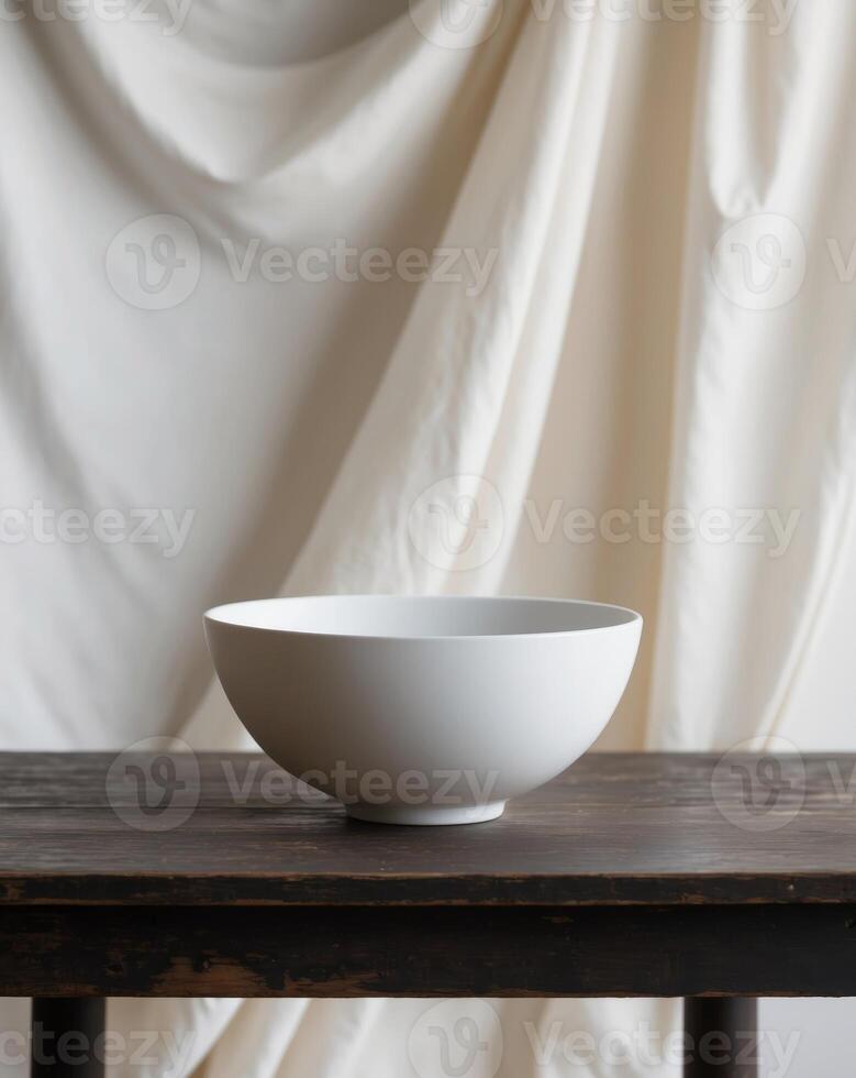 Simple white bowl placed on a wooden table with soft fabric in the background photo
