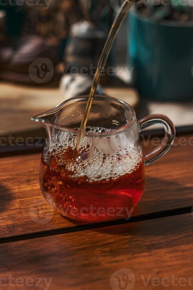 Rich Tea is being poured elegantly into a beautiful glass jug placed on a rustic wooden table photo