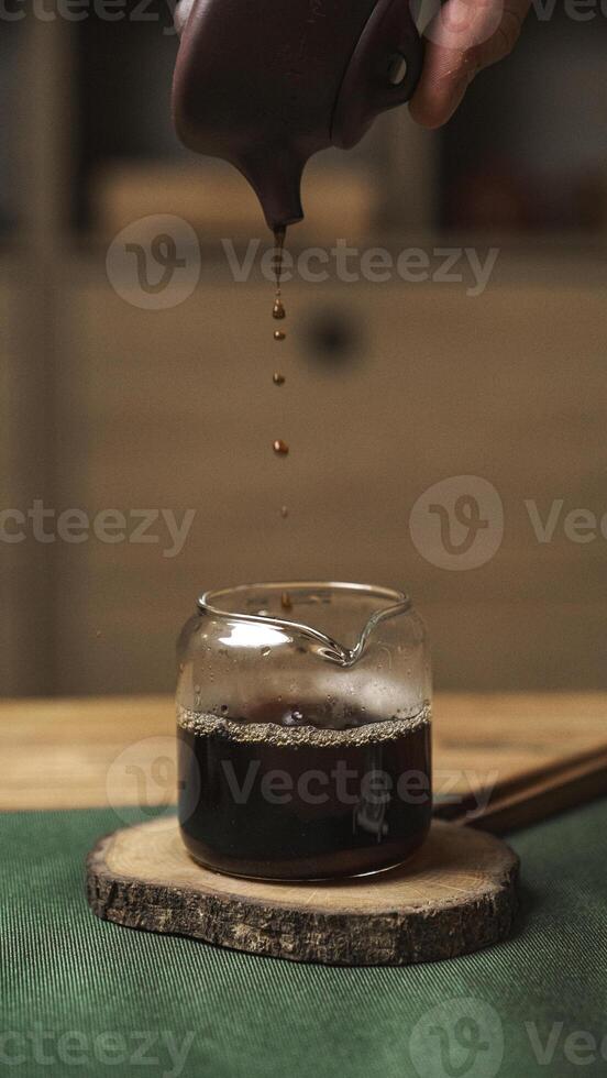 Carefully pouring a rich and dark syrup into a lovely glass jar that sits on a rustic wooden slice photo