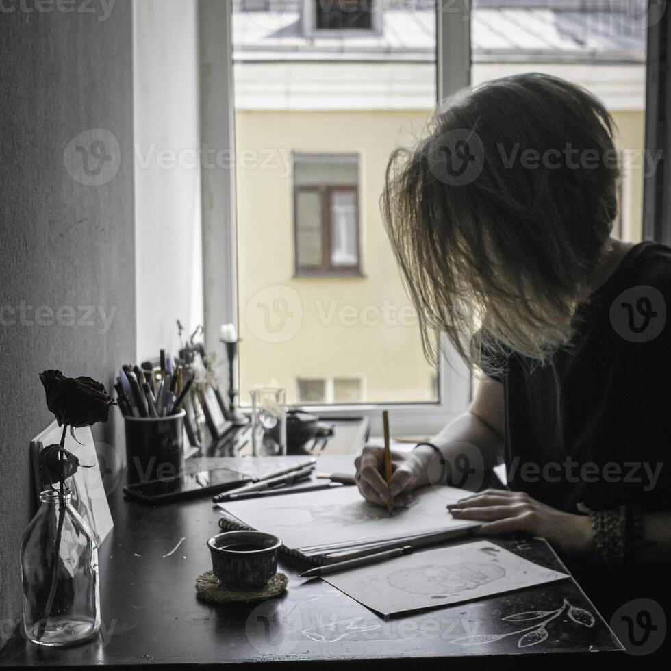 A creative workspace featuring an artist at their desk engaged in the act of drawing thoughtfully photo
