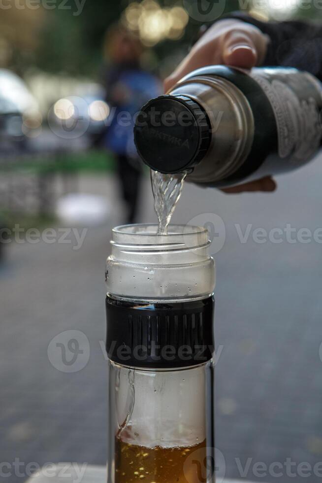 Carefully pouring a drink from a thermos into a glass bottle while enjoying the outdoors photo