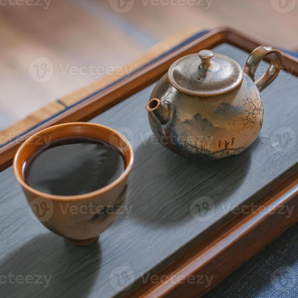 A beautiful and traditional tea pot along with a cup is elegantly placed on a wooden tray photo