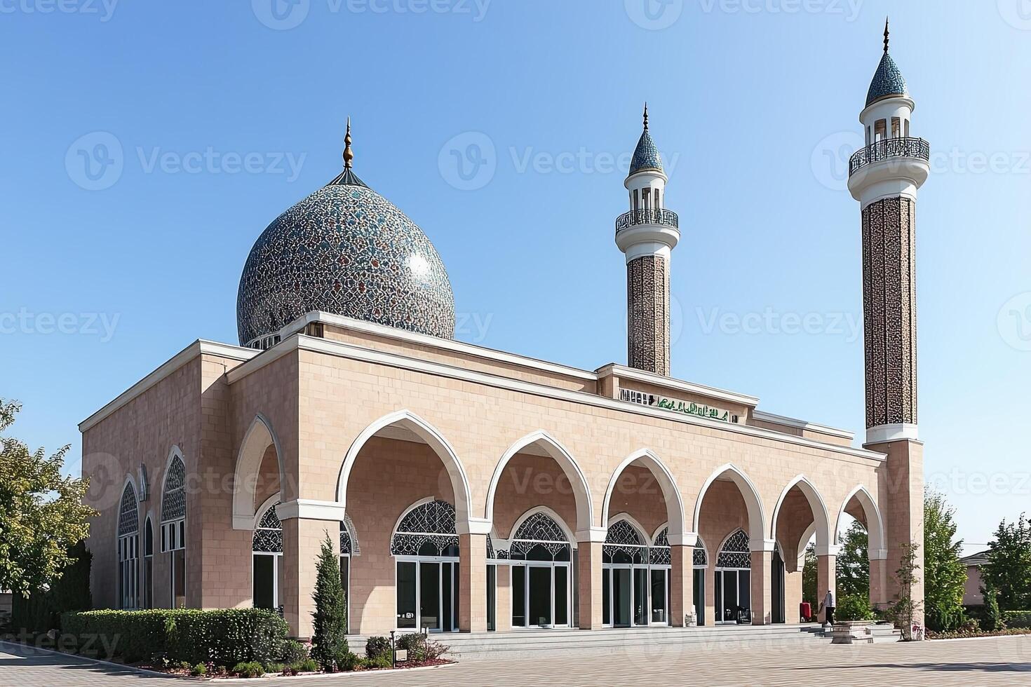 Grand mosque with arched entryway, two minarets, and a patterned dome under a clear sky. photo