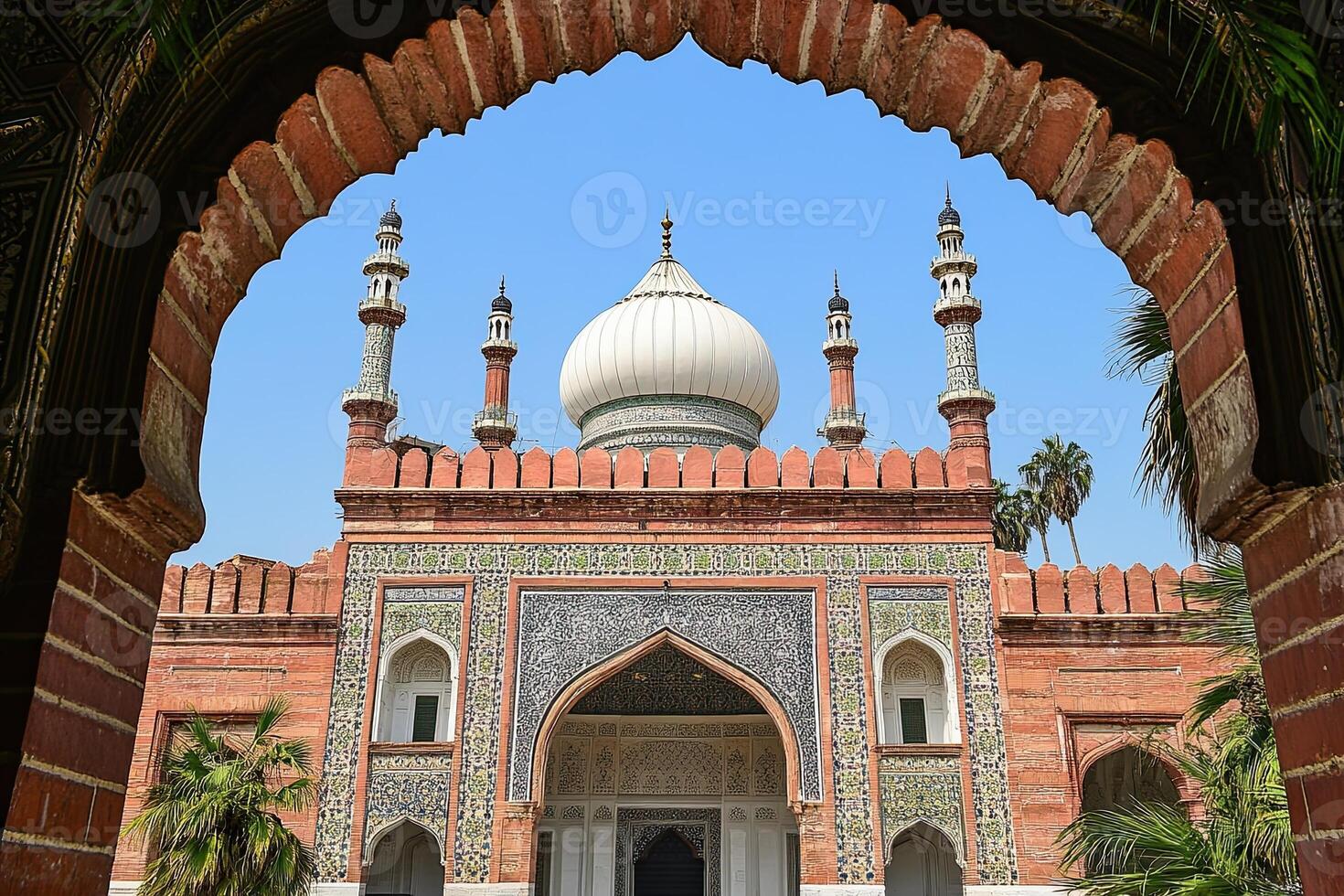 Framed view of a grand mosque with intricate details, white dome, and red brick facade under a clear blue sky. photo