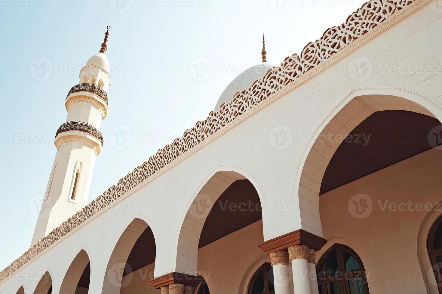 Low angle view of a white mosque with arches and minaret under a clear sky. photo