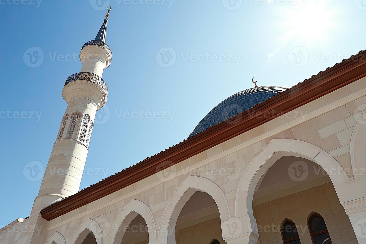 Low-angle view of a mosque's minaret and dome under a clear blue sky. photo