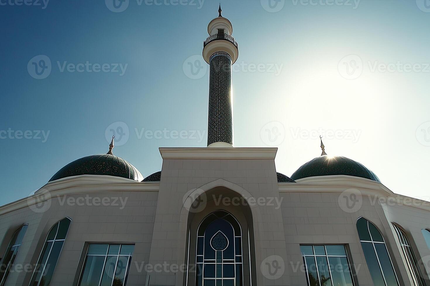 Low angle view of a mosque with two green domes and a tall minaret under a bright blue sky. photo