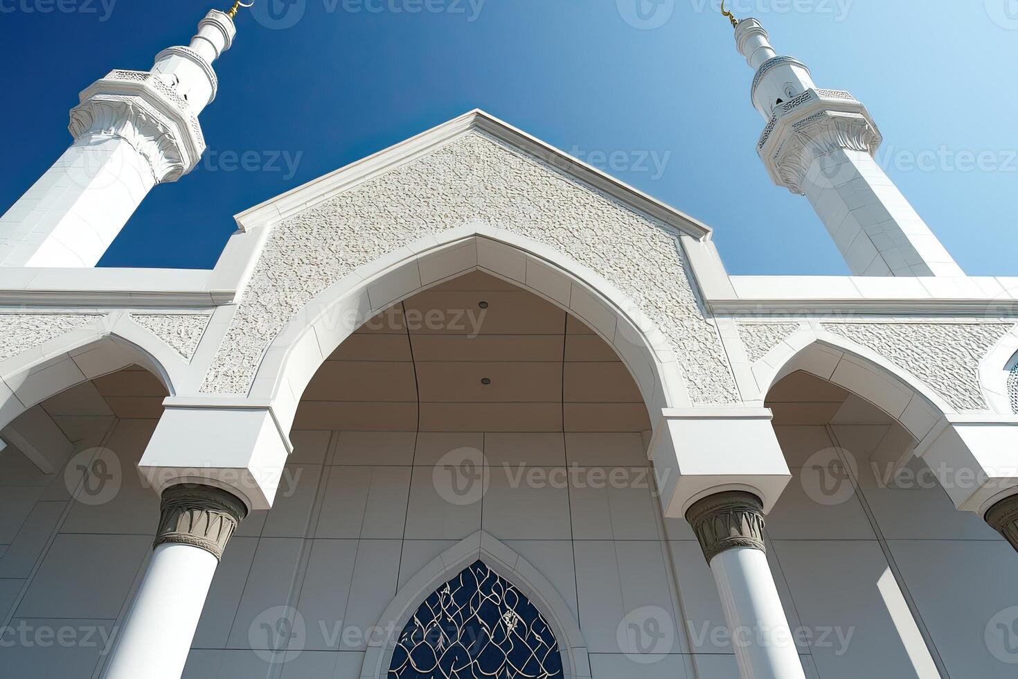 Low-angle view of a white mosque with intricate details, two minarets, and a clear blue sky. photo