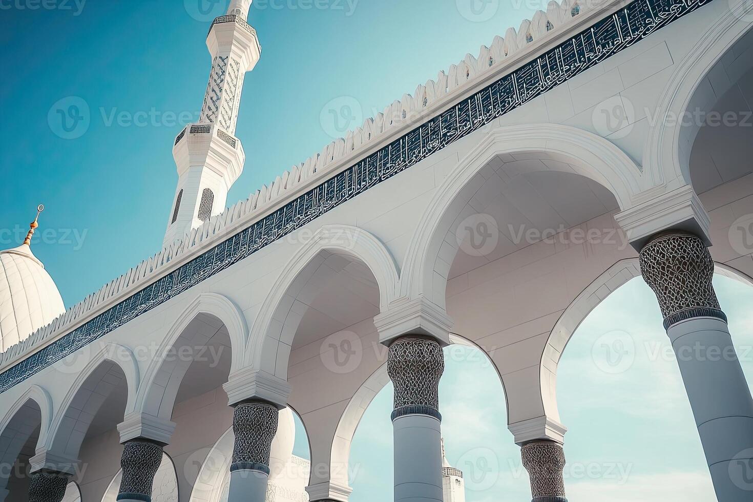 Low-angle view of white mosque architecture, intricate details, arches, minaret against blue sky. photo