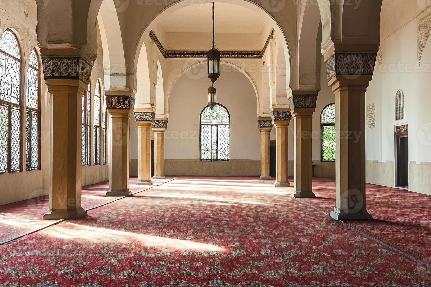 Sunlit mosque interior with arched columns, ornate pillars, and red carpet. photo