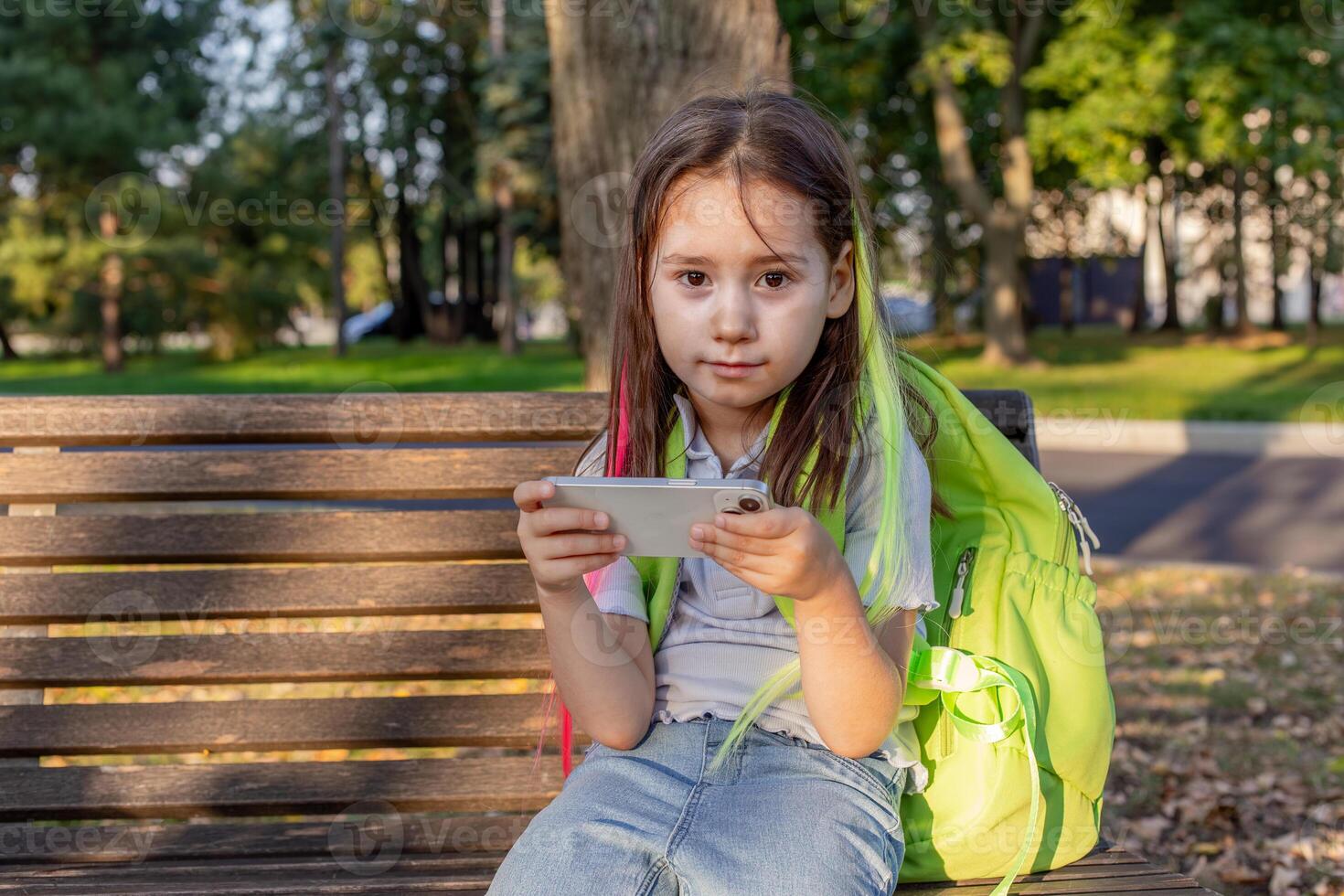 Girl on park bench using smartphone with backpack in autumn photo