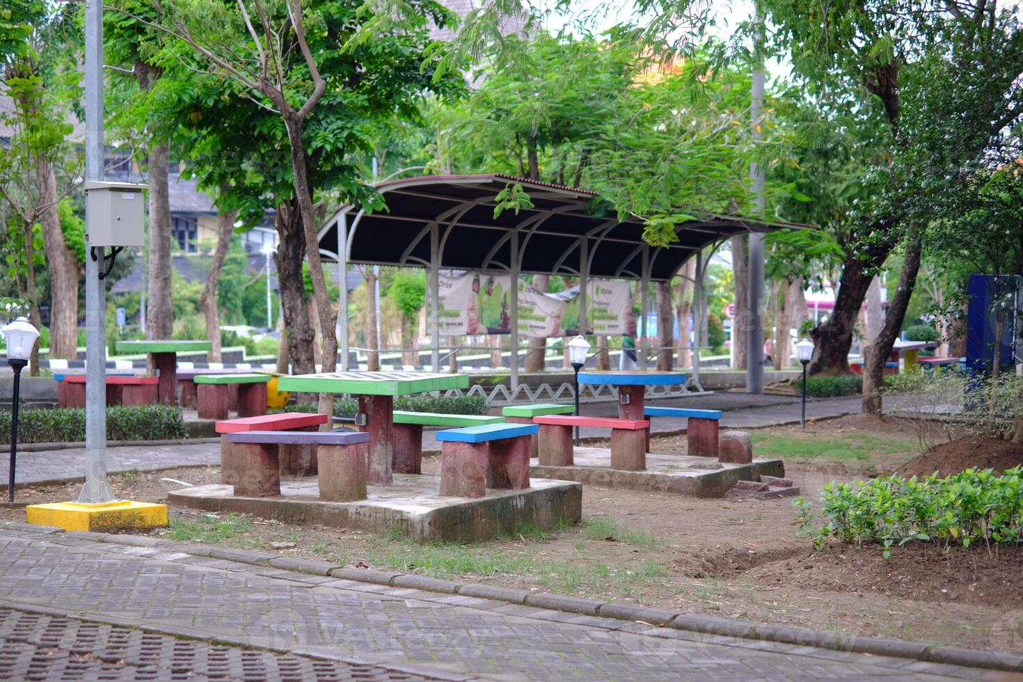 a vibrant garden setting featuring colorful picnic tables in the shade surrounded by lush greenery and shady trees. photo