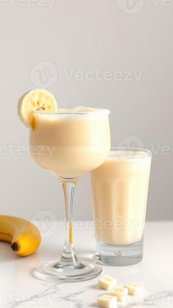 Creamy banana smoothie served in a stylish glass along with a refreshing beverage on a marble countertop photo