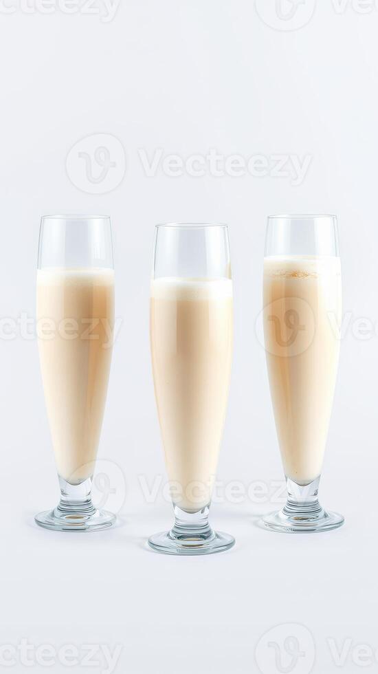Three elegant glasses of creamy beverage stand in a row on a plain background, showcasing a light tan hue photo