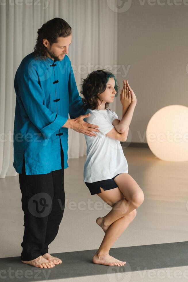 A yoga instructor in training helps a child to do exercises in the gym photo