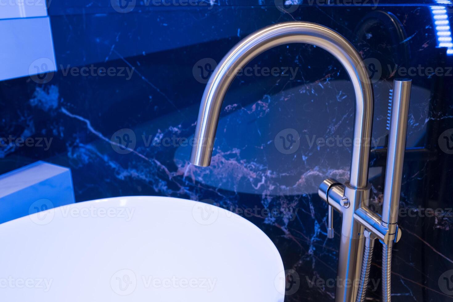 Closeup of silver bathroom faucet in bathroom next to white tub. Chrome faucet against a black granite wall photo