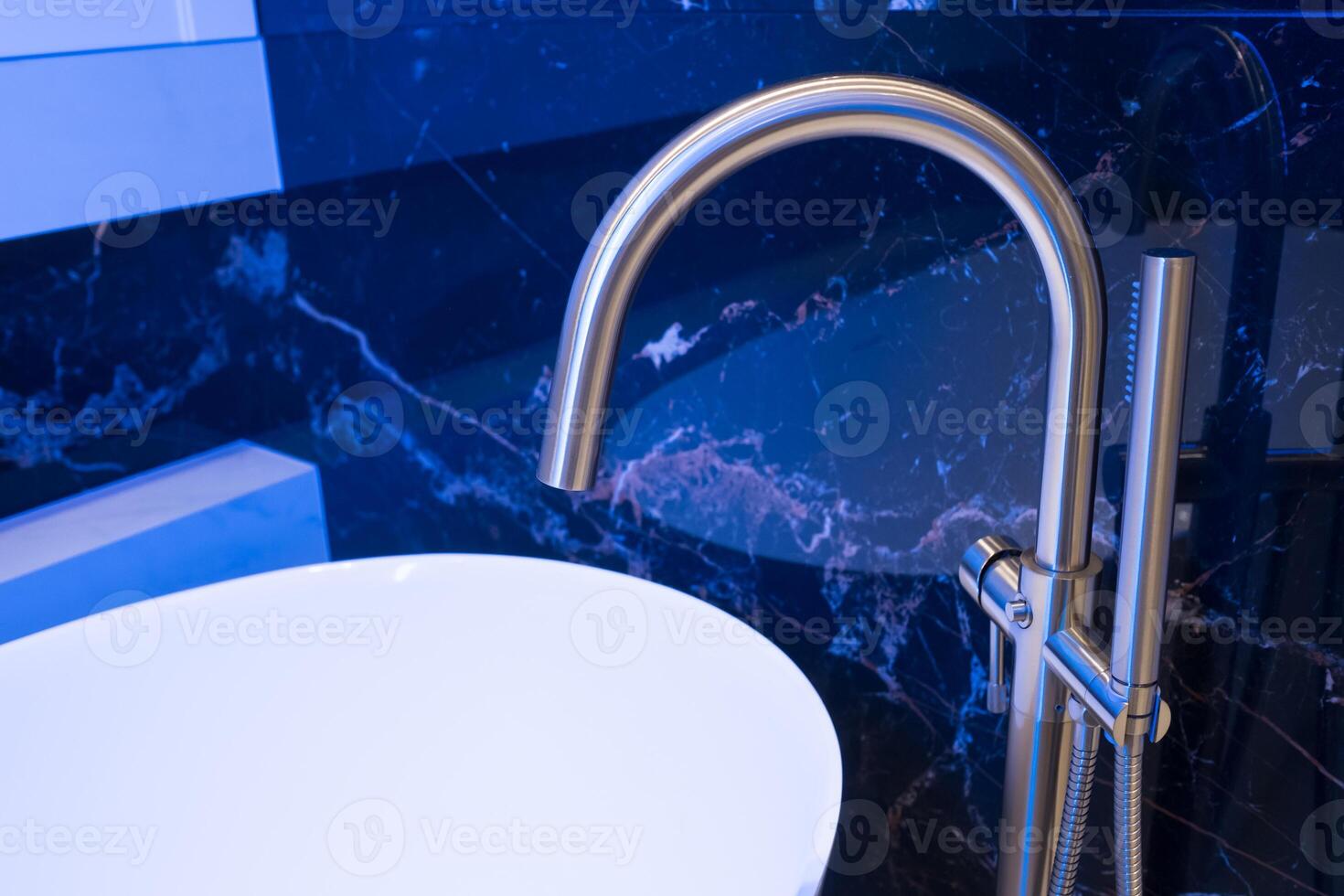 Closeup of silver bathroom faucet in bathroom next to white tub. Chrome faucet against a black granite wall photo
