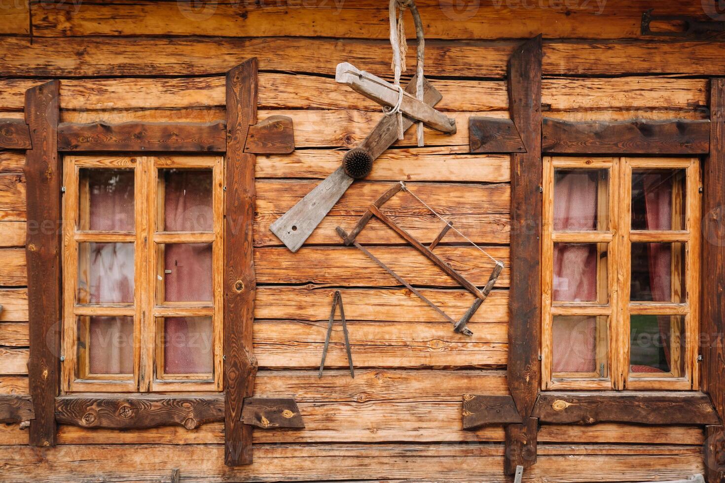 An old wooden wall of a house with windows in the village and tools hanging photo
