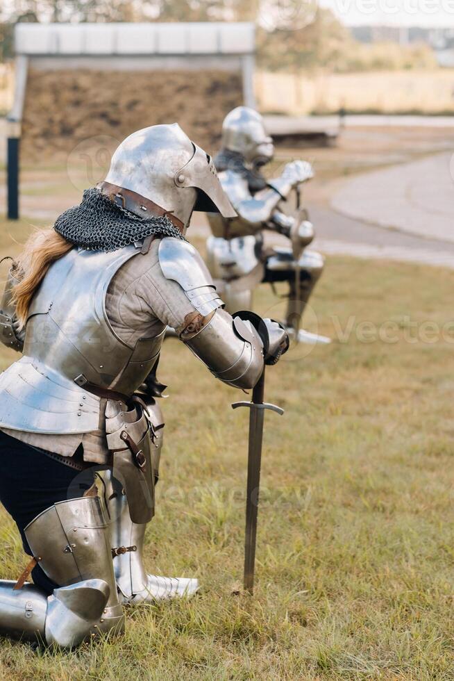 two knights in ancient metal armor stand at the stone wall of the castle photo