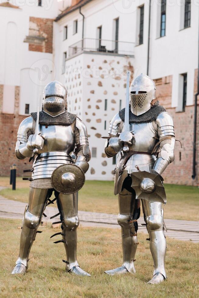 two knights in ancient metal armor stand at the stone wall of the castle photo