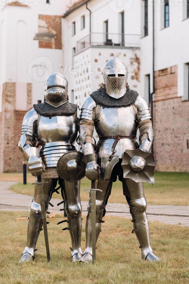 two knights in ancient metal armor stand at the stone wall of the castle photo