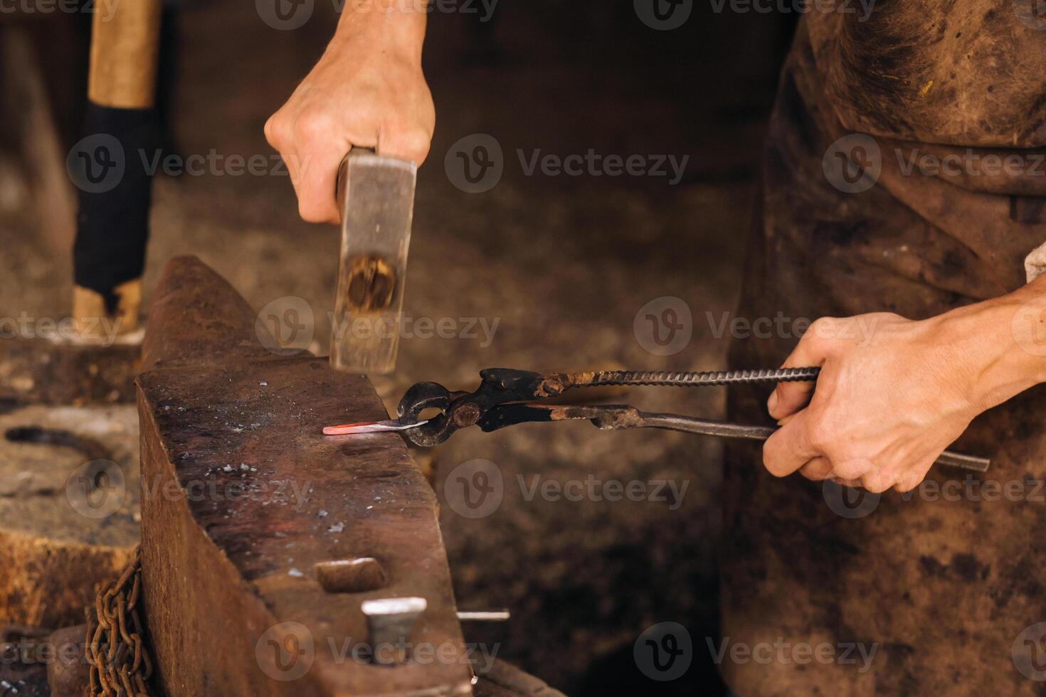 A blacksmith manually forges red-hot metal on an anvil with a hammer photo